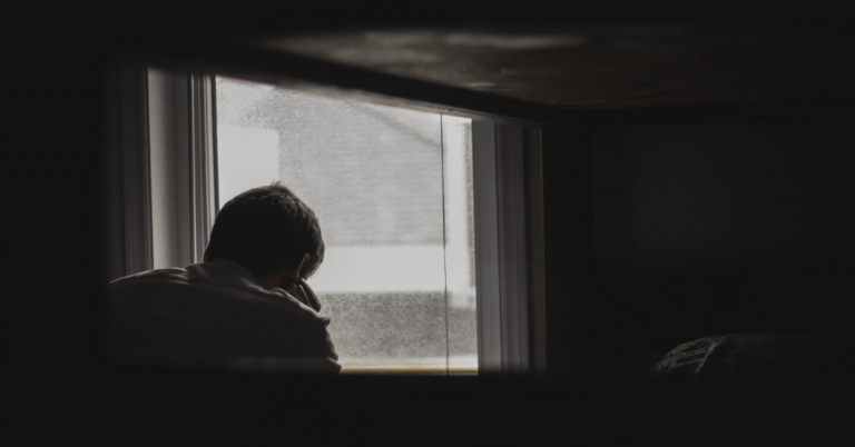 Man sitting in dark room, head in hands, depressed, sad